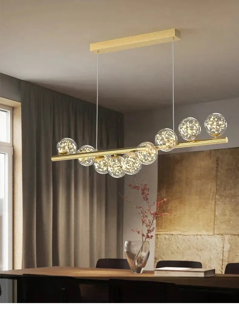 Nordic ceiling chandelier with a gold brass bar and multiple clear glass globe bulbs, suspended by two cables.