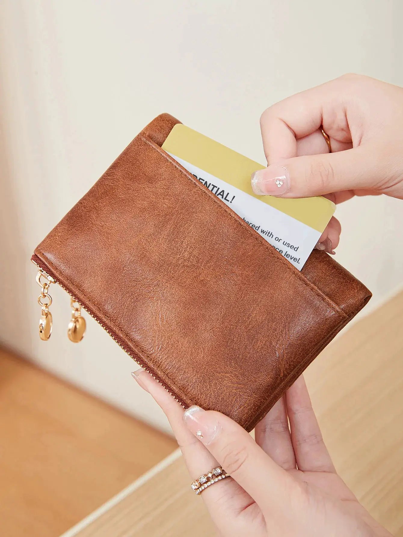 Brown leather minimalist wallet with double gold zippers, hand inserting a card.