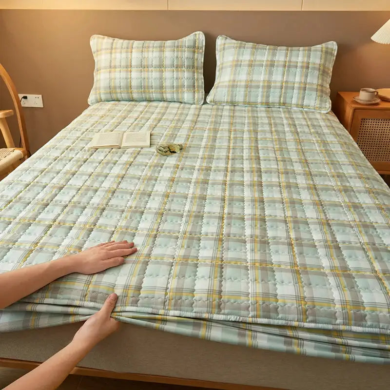 Quilted plaid mattress cover protector in pastel blue-green with yellow lines; breathable and antibacterial