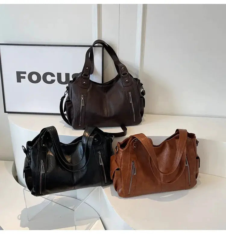 Set of three PU leather shoulder bags in black, brown and tan with front zipper pockets and top handles.