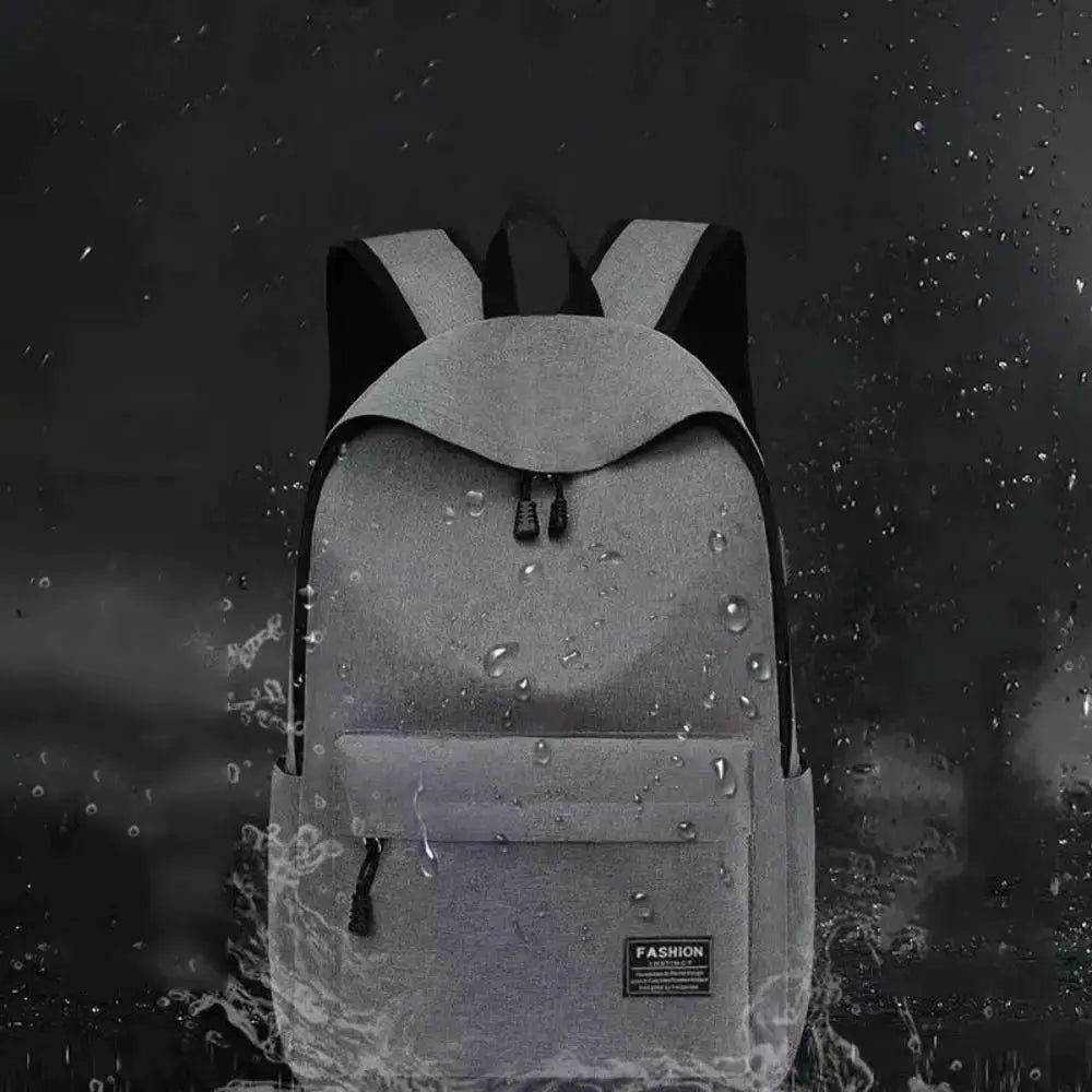 Gray minimalist backpack with front zip pocket and black straps, water droplets on the surface, versatile everyday bag.