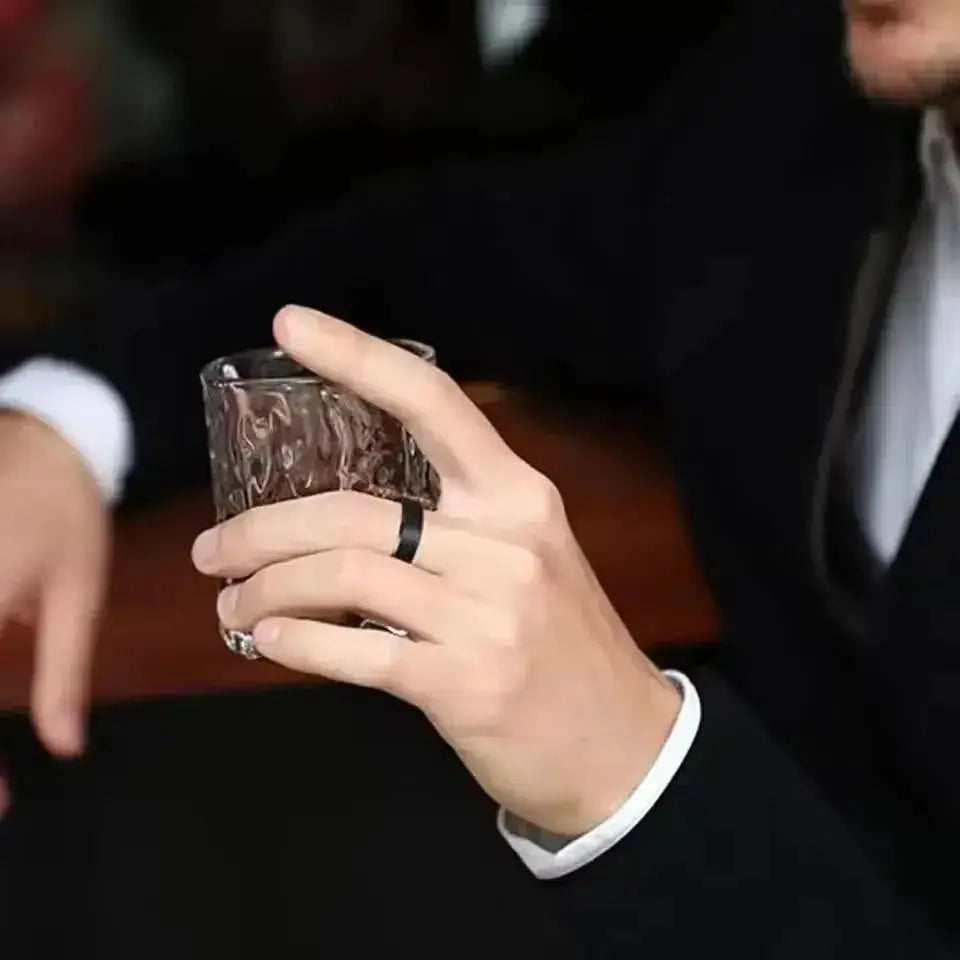 Unisex stainless steel ring with black matte finish worn on a hand holding a glass.