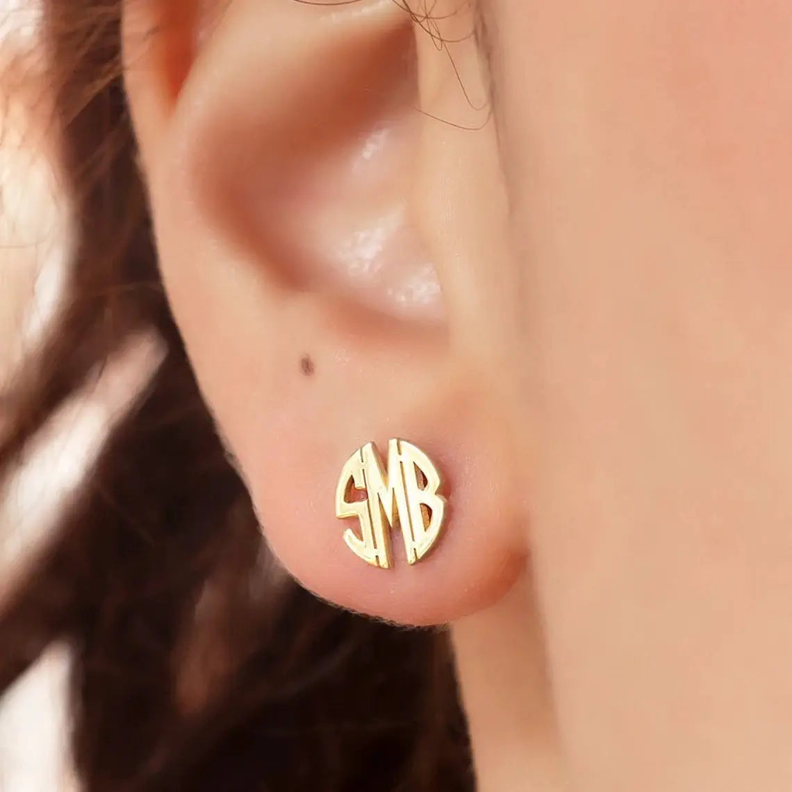 Gold-tone round monogram stud earring with SMB initials on the earlobe