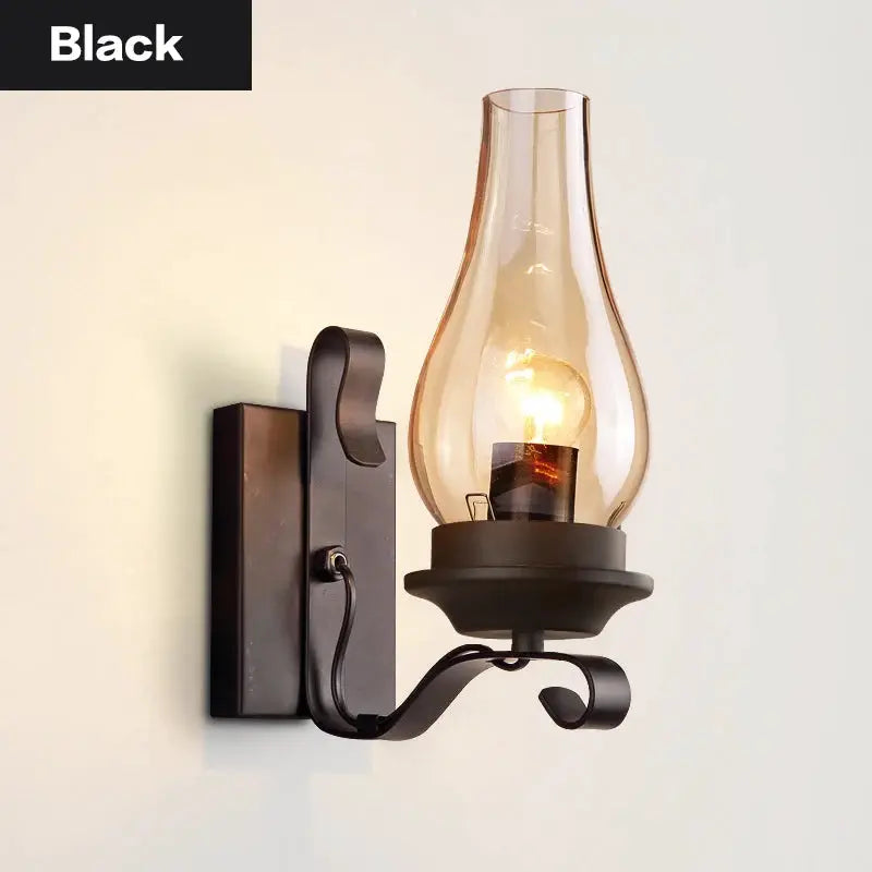 Wall lamp in black wrought iron with a curved arm and clear glass hurricane shade