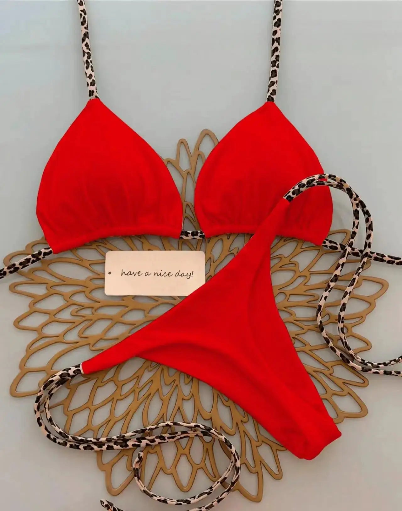 Red bikini set with leopard-print straps and triangle top; thong-style bottom.