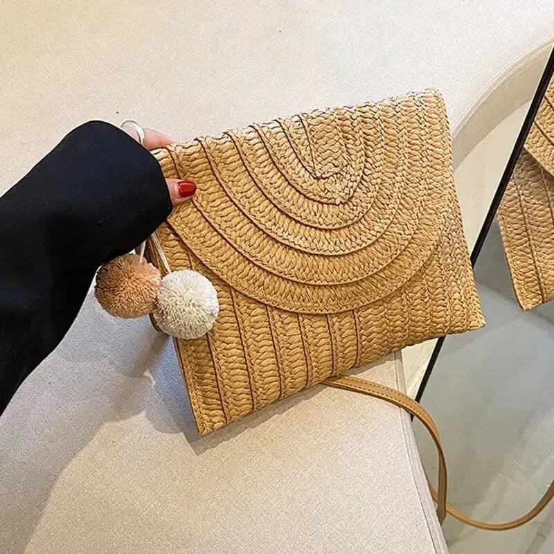 Handmade straw beach crossbody bag by Simples Market; envelope-woven design in beige with pom-pom charms