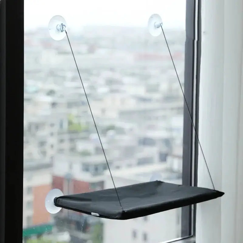 Cat hammock bed by Simples Market, black fabric, mounted to a sunny window with suction cups