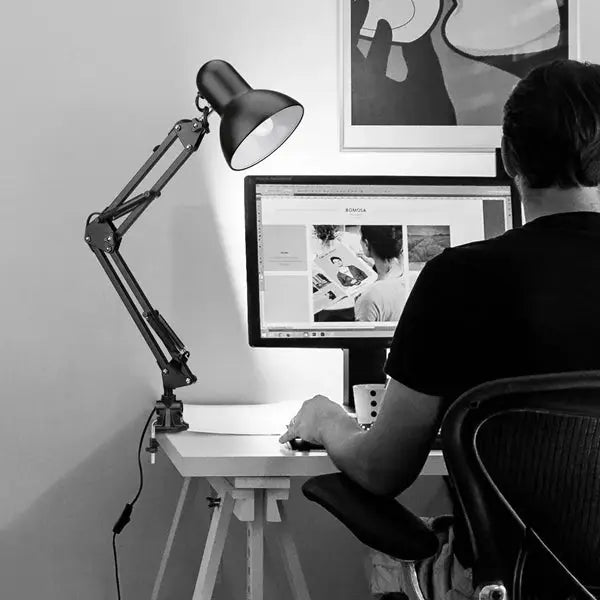 Swing arm clamp lamp by Simples Market, black metal desk light with adjustable arm and shade beside computer monitor