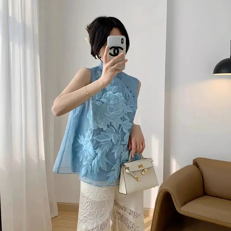 Blue floral-embroidered cheongsam top; white lace pants and beige handbag create a three-piece look with Chanel case.