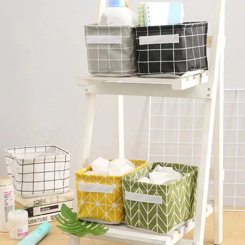 Linen storage baskets; five on a shelf in grey/black/white grid patterns, yellow geometric and green leaf patterns.