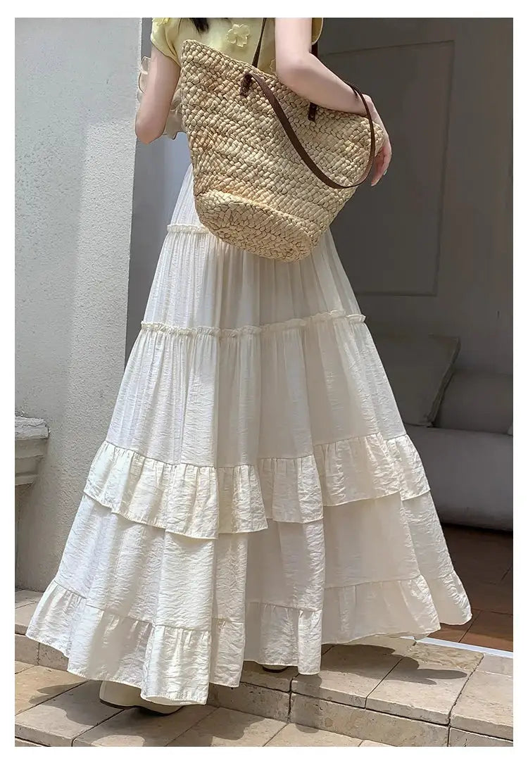 White tiered ruffle-hem maxi skirt with high waist, paired with a woven straw tote bag