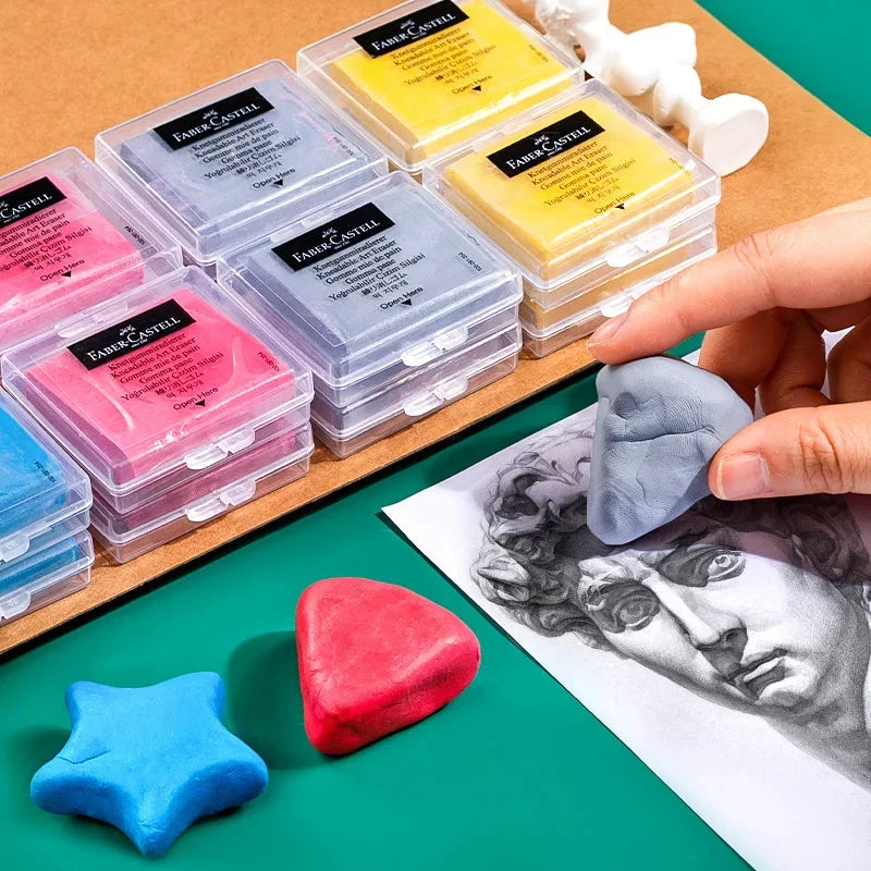 Faber-Castell kneaded erasers in clear cases, assorted colors, with blue star and red heart erasers on a green surface.
