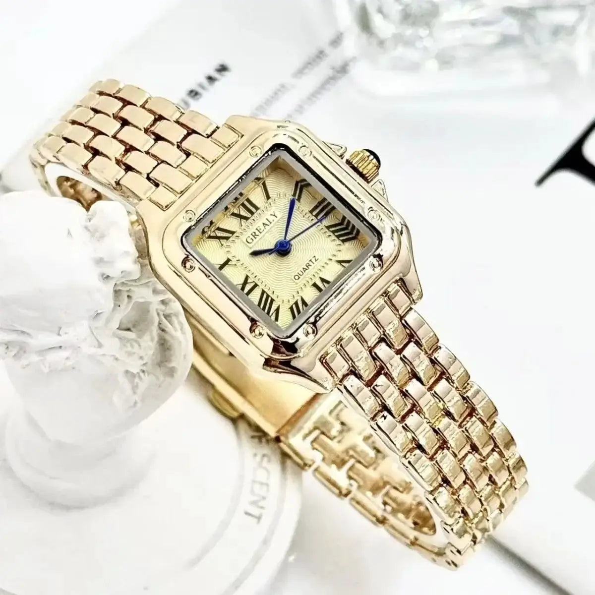 Gold-tone square-shaped women's quartz watch with rhinestone bezel, blue hands, and linked bracelet
