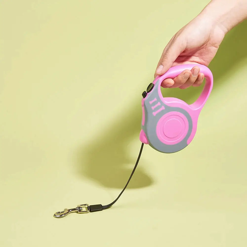 Pink retractable dog leash with gray housing and black cord, handheld with metal clip