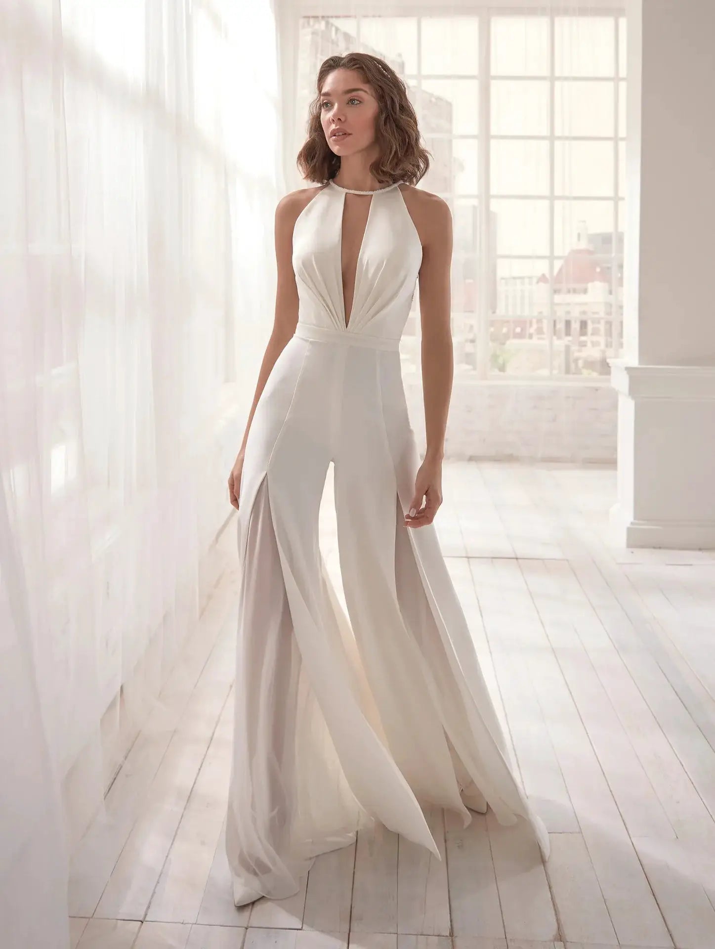 White halter-neck jumpsuit with deep V neckline, sleeveless backless design and wide-leg flowing pants.