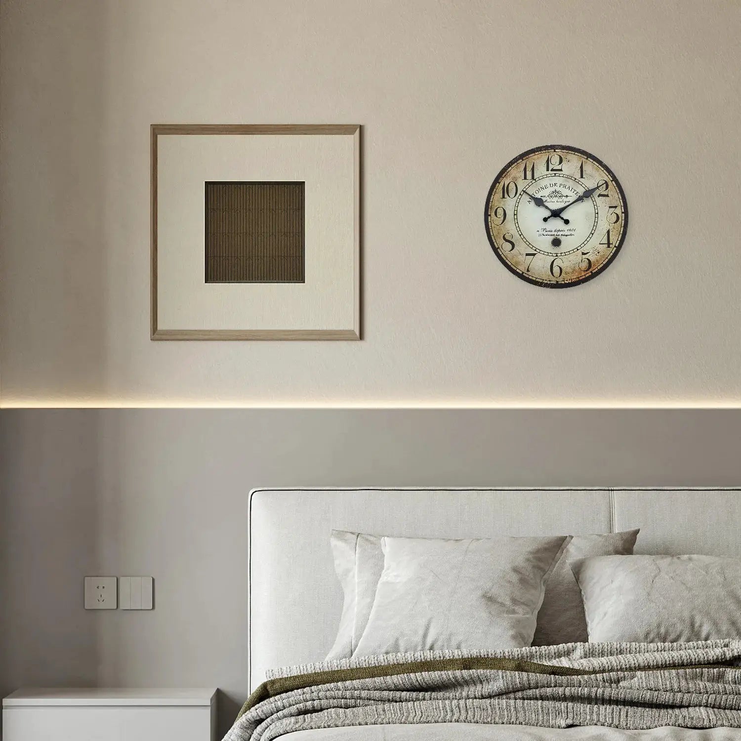 Vintage round wall clock with antique beige dial displayed beside a square framed art on a beige wall