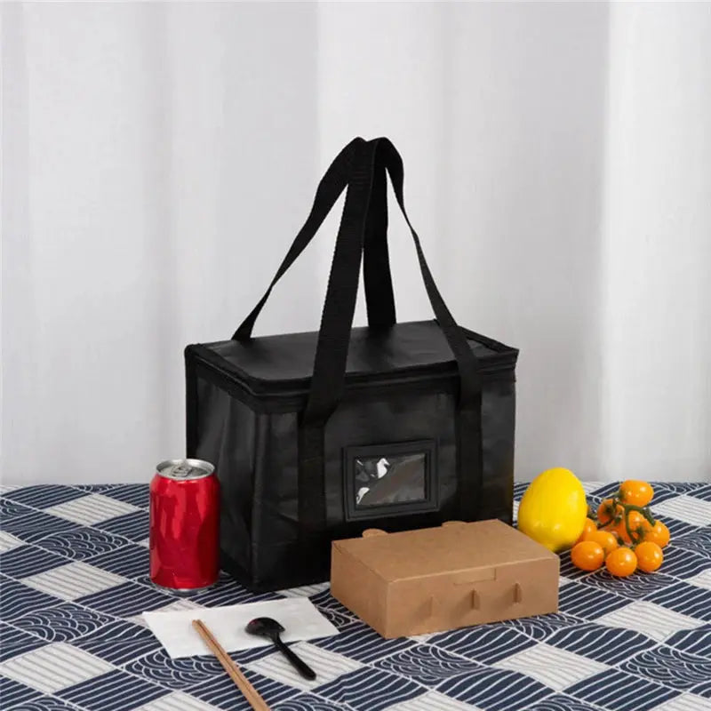 Simples Market black portable large insulated food delivery bag with handles and viewing window beside red can and fruit