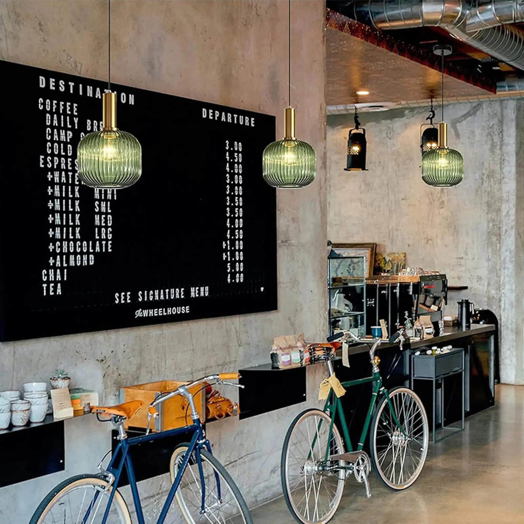 Nordic glass pendant lights with green ribbed shades and brass tops hung in a cafe interior set of 2