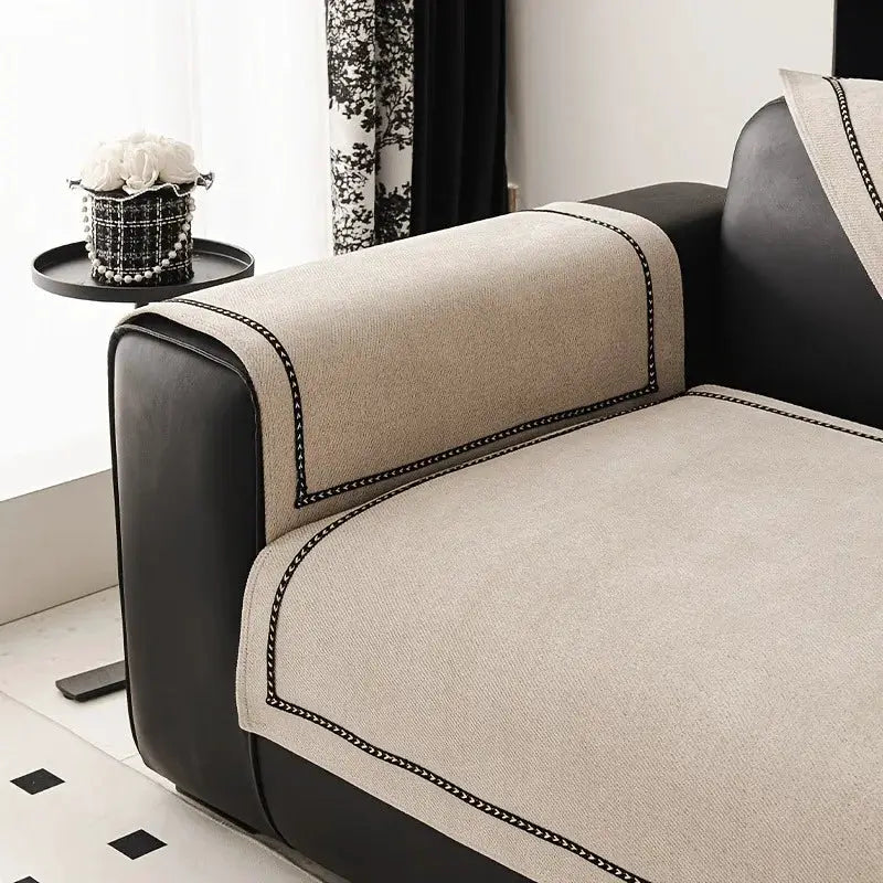 Sofa slipcover in beige chenille with black trim on a black leather sofa