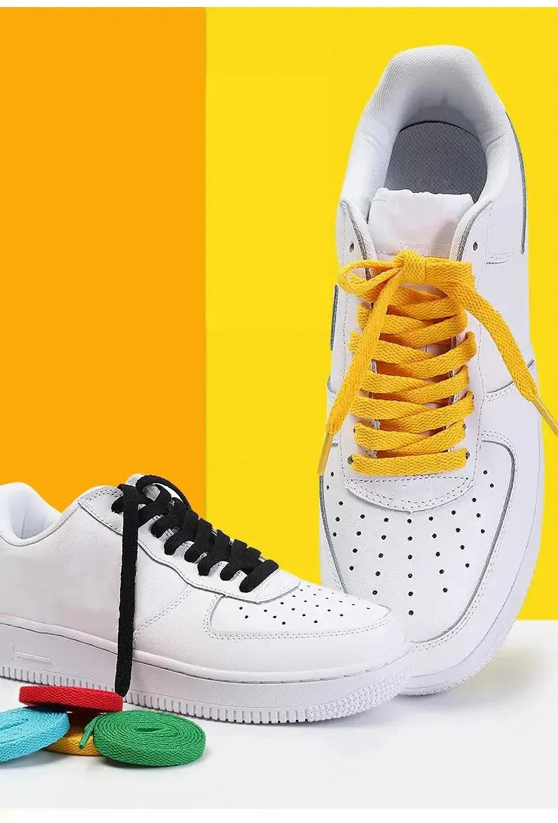 Flat sneaker shoelaces; yellow lace on right shoe and black lace on left, with colorful spools in foreground