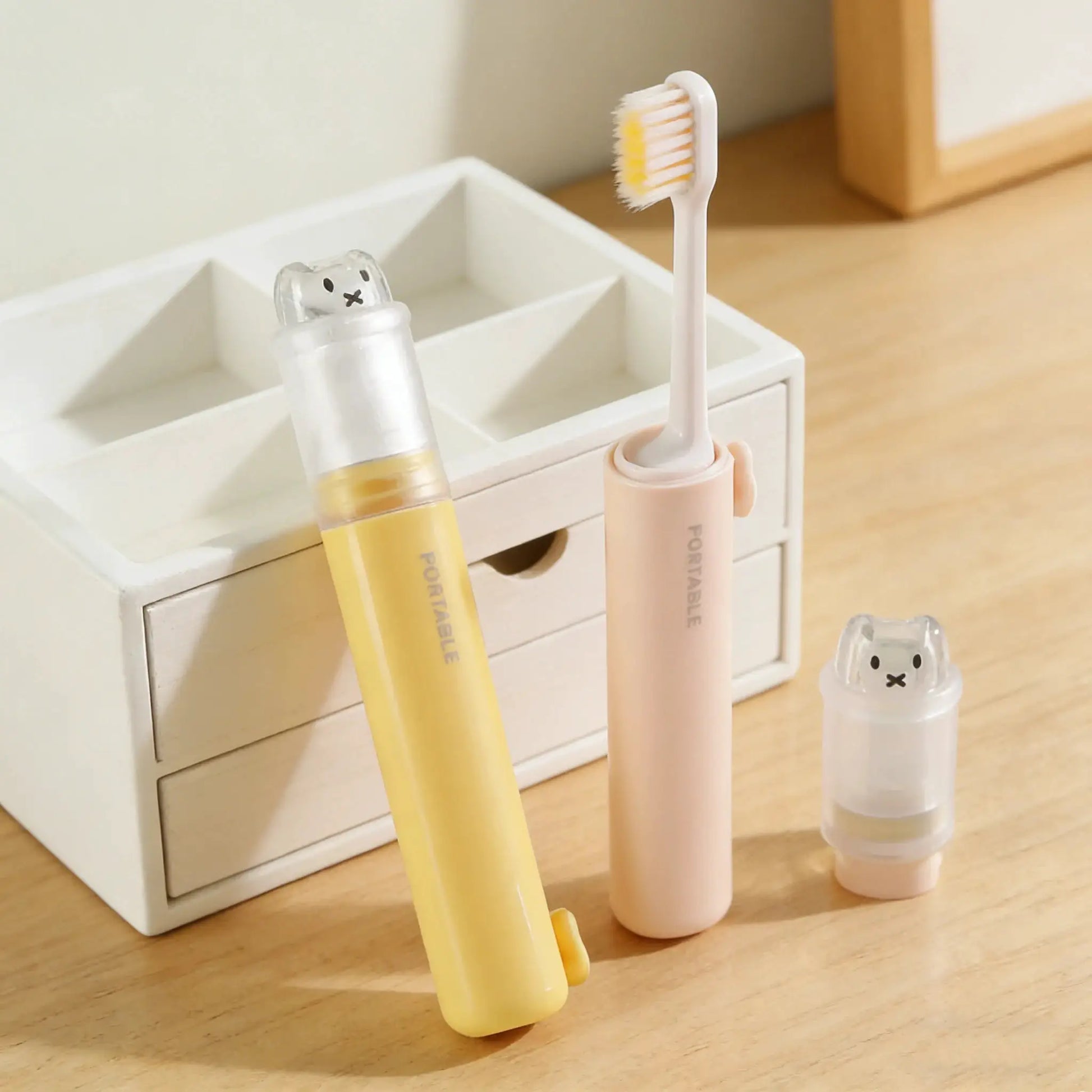 Simples Market 2-in-1 foldable travel toothbrush set with toothpaste storage; two pastel yellow and pink brushes, bear dust cover