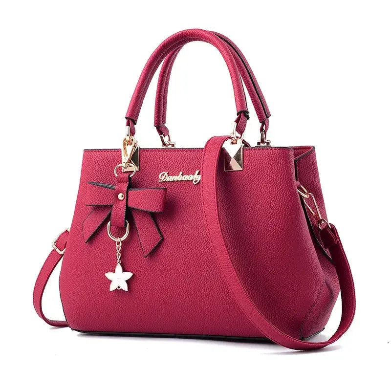 Handbag in pink pebble texture with front bow, star charm, double top handles, and shoulder strap