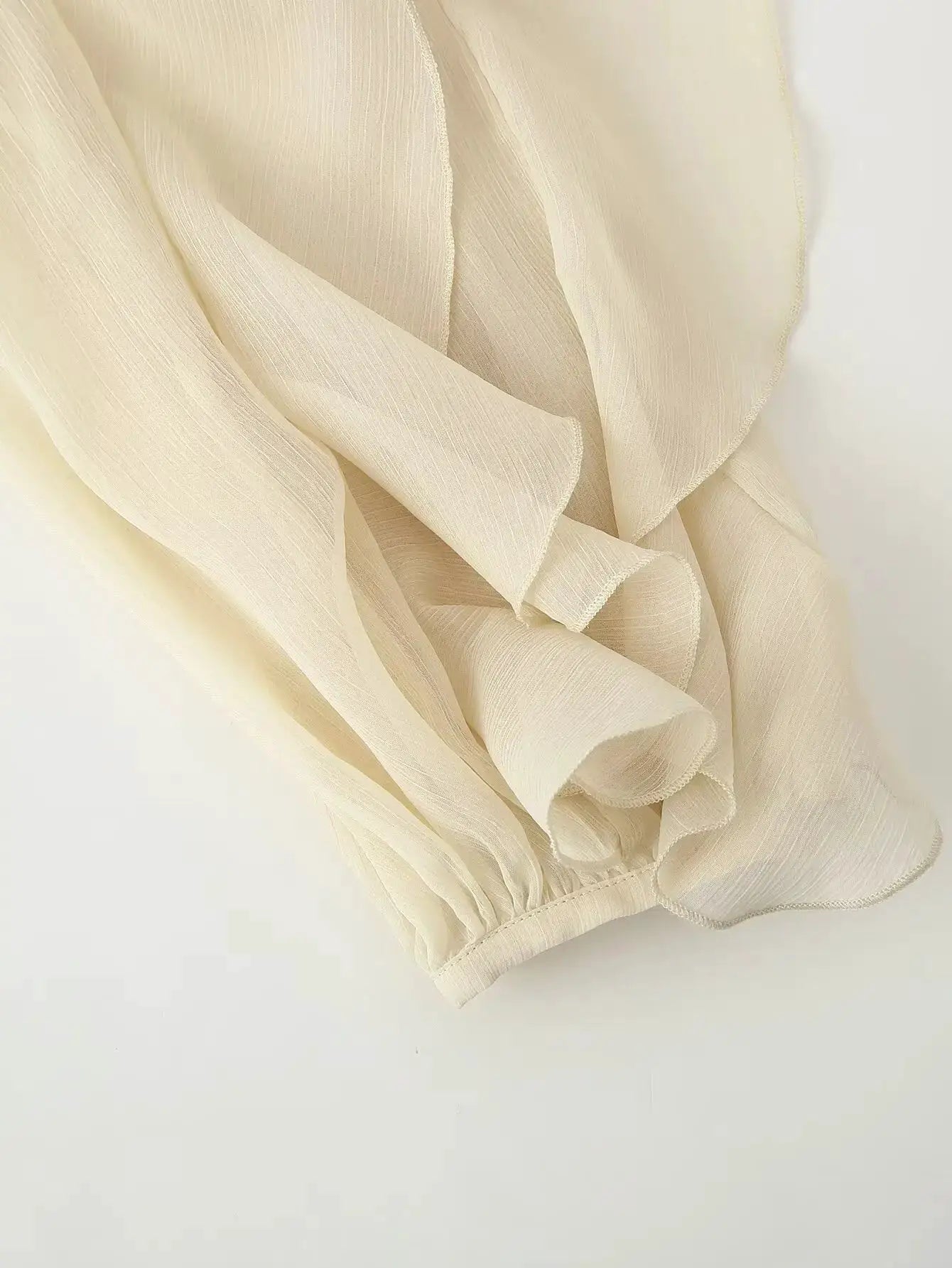 Women’s blouse close-up in cream semi-sheer fabric with subtle vertical stripes and elastic cuff.