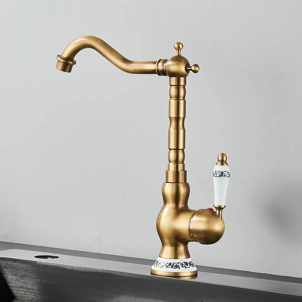 Antique brass bathroom faucet with rotating spout, ceramic handle and ornate base.
