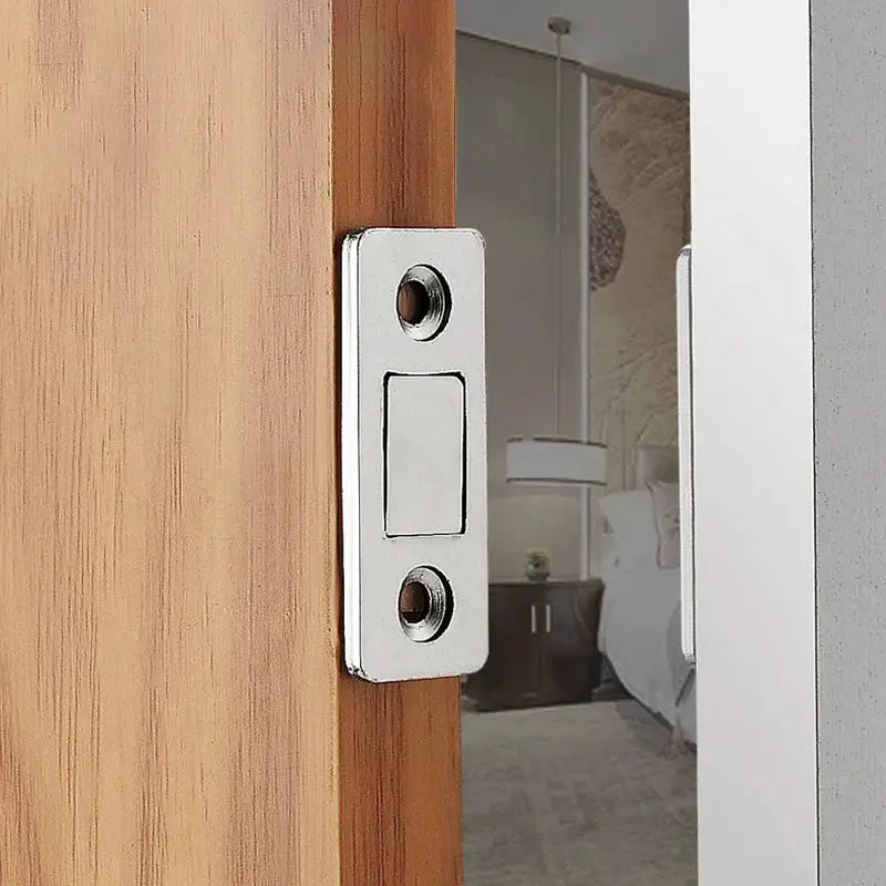Slim chrome magnetic cabinet catch on a wooden door edge with two screw holes.