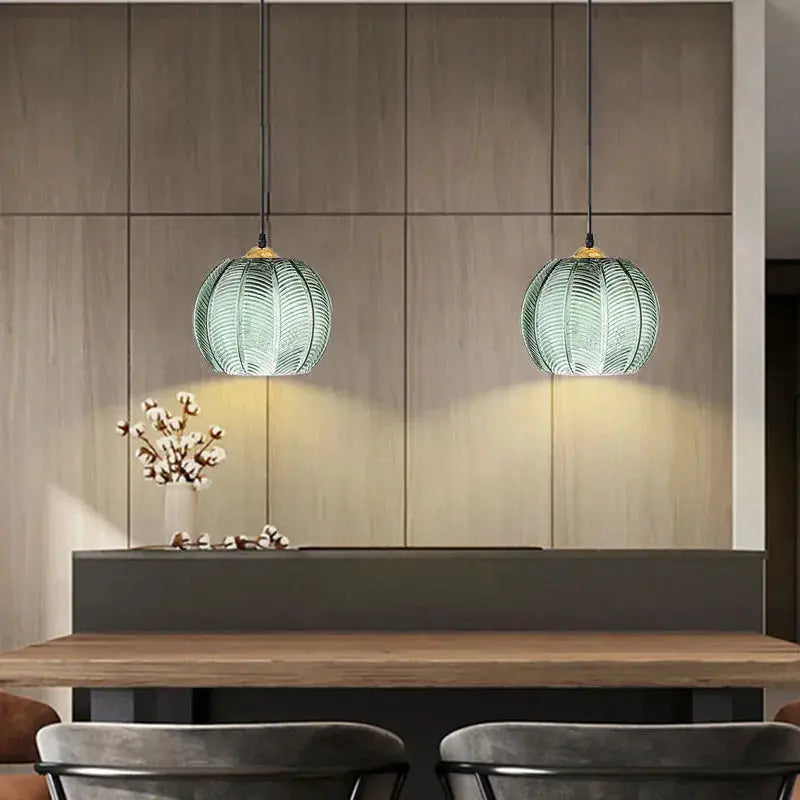 Nordic glass pendant lights with green leaf pattern, two hanging above a wooden dining table.