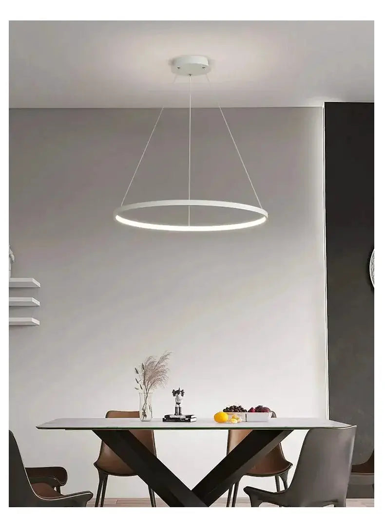 Modern round LED pendant light, white ring, suspended above a dining table in a minimalist dining space.