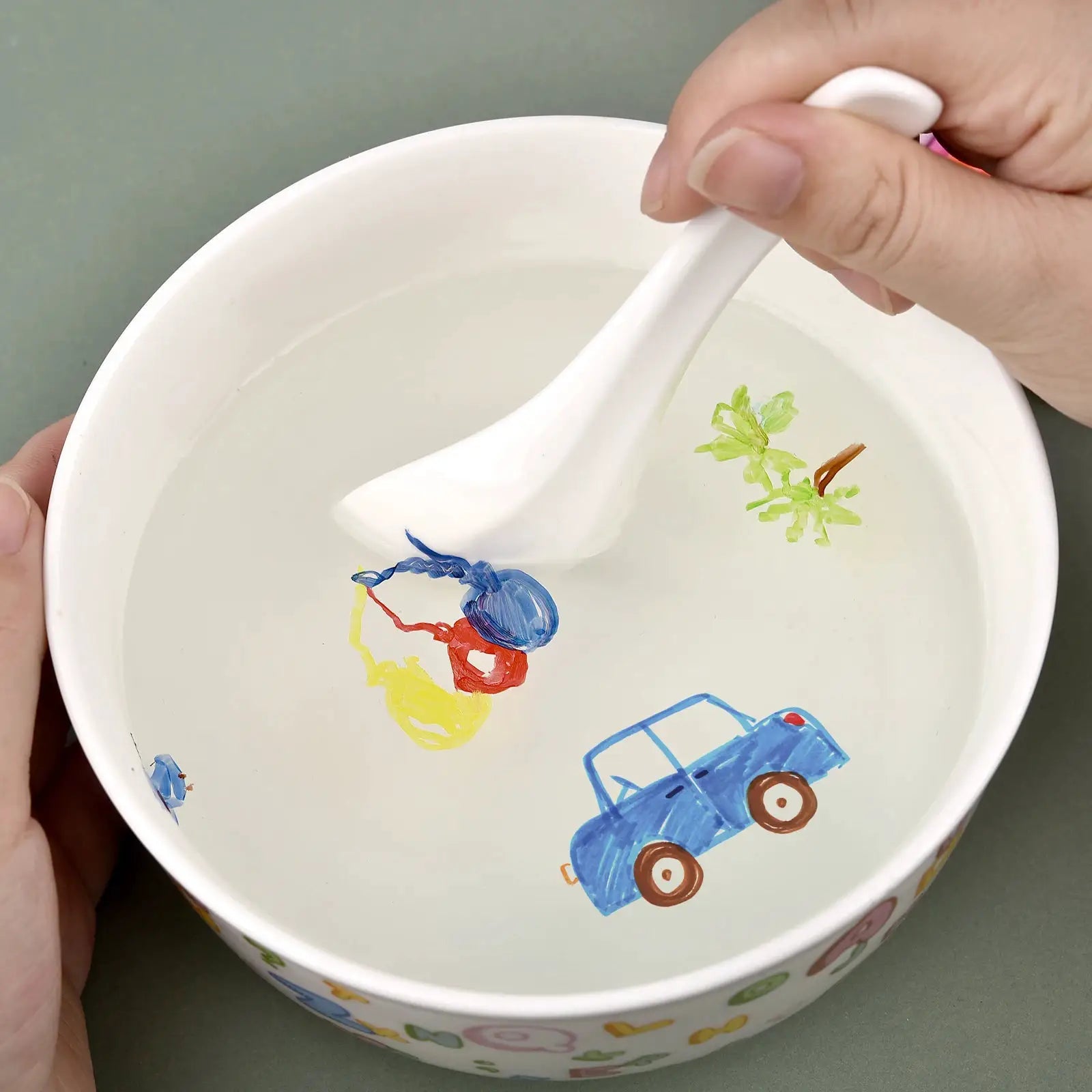 Magical water painting pen, white, in a white bowl of water with colorful blue car and green plant drawings