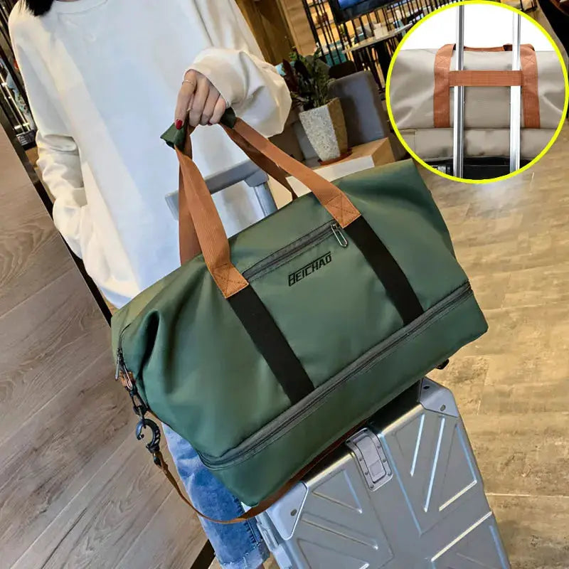 Green travel gym bag with brown handles and black straps on a silver rolling suitcase