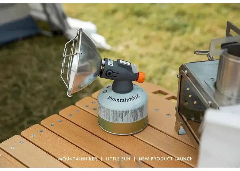 Mountainhiker portable mini sun gas stove with green canister and metal reflector on a wooden outdoor camping table