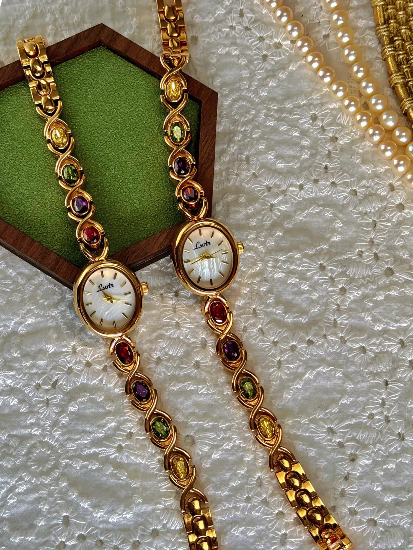 Two gold-tone luxury women's watches with rainbow tourmaline stones on bracelet links and oval mother-of-pearl dials.