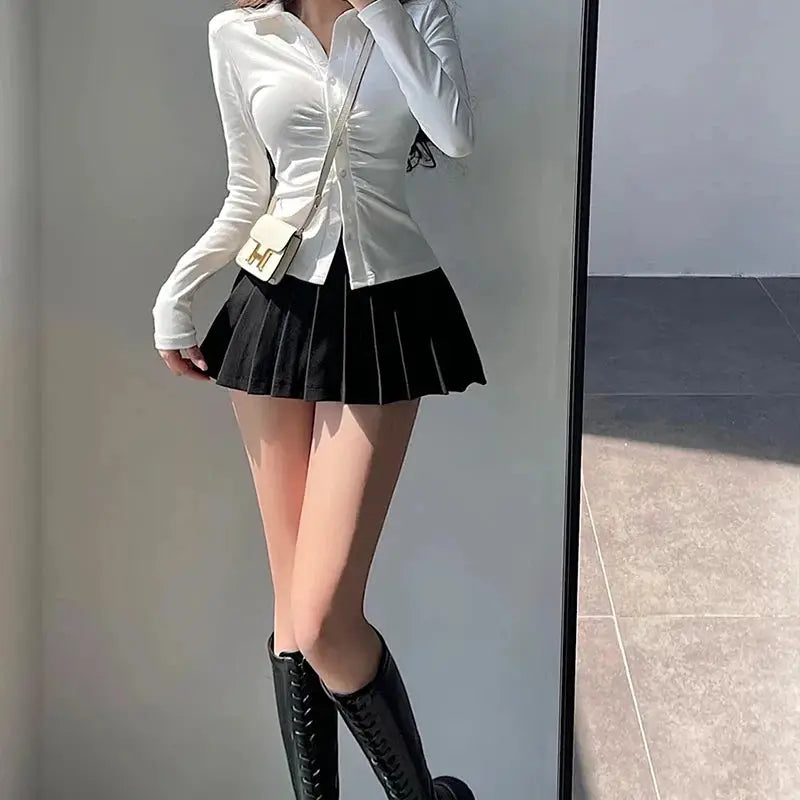 Pleated black high-waist mini skirt, shown with white blouse and knee-high boots