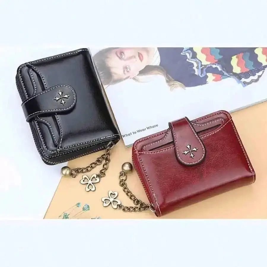 Two women's mini leather wallets in black and burgundy with strap and chain accents and star emblem.