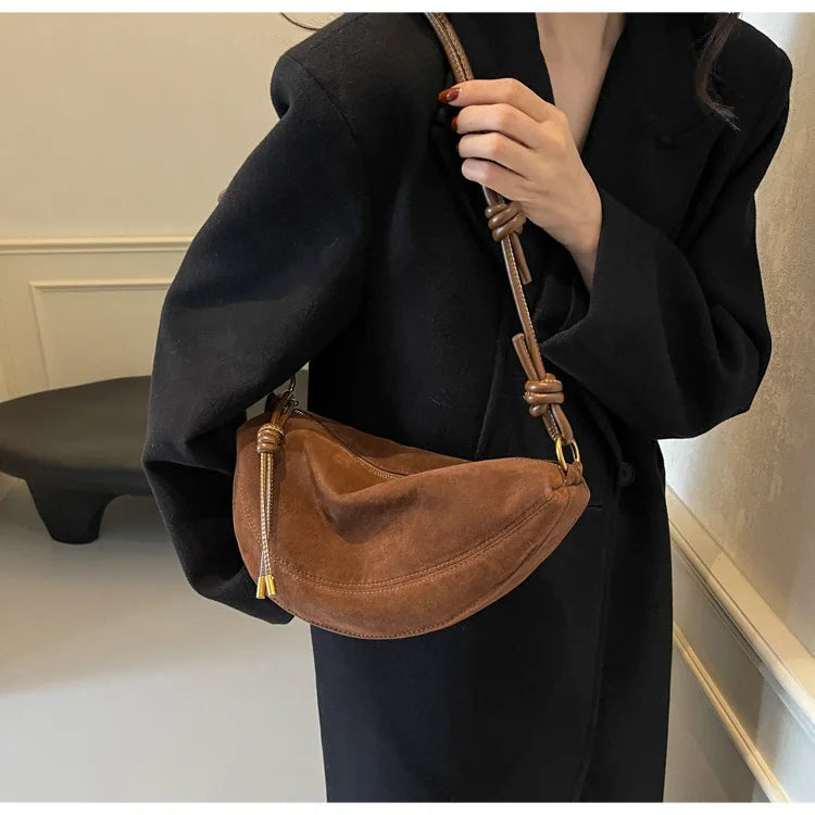 Brown faux suede shoulder bag with adjustable crossbody strap worn by a woman in a black coat