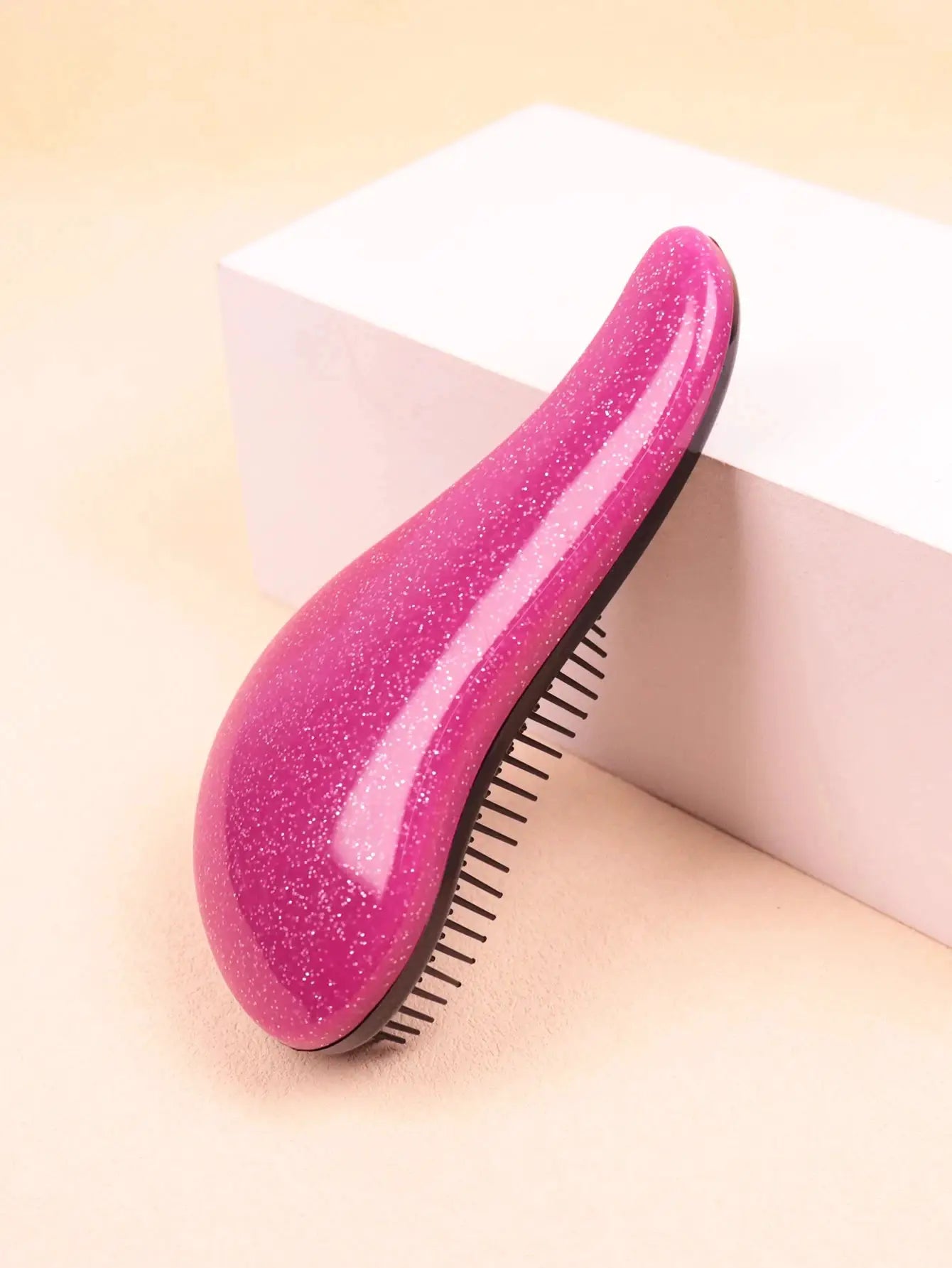 Smoothing wig brush by Simples Market, pink glitter curved design with black teeth.