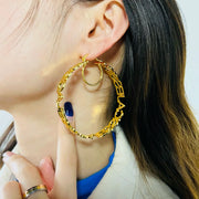 Gold-tone large hoop earrings with textured cutout pattern worn by a woman