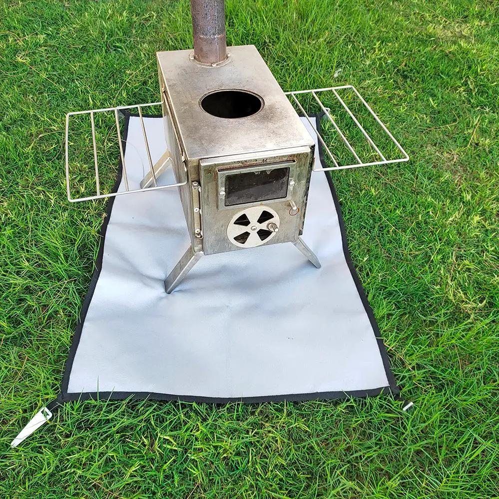 Camping Fireproof Cloth BBQ Grill Mat in gray with black edge beneath a metal camping stove with side racks on grass