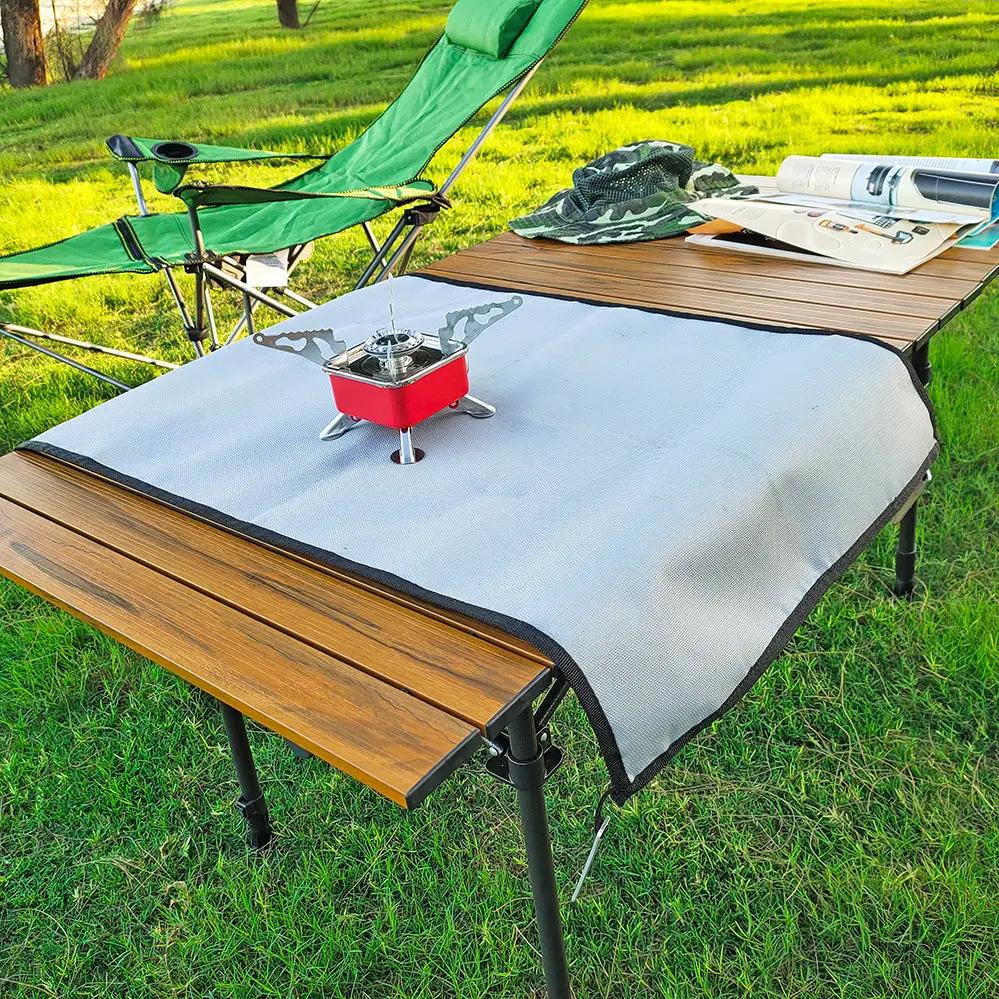 Camping fireproof cloth BBQ grill mat in gray heat-resistant fabric under a portable stove on an outdoor table.