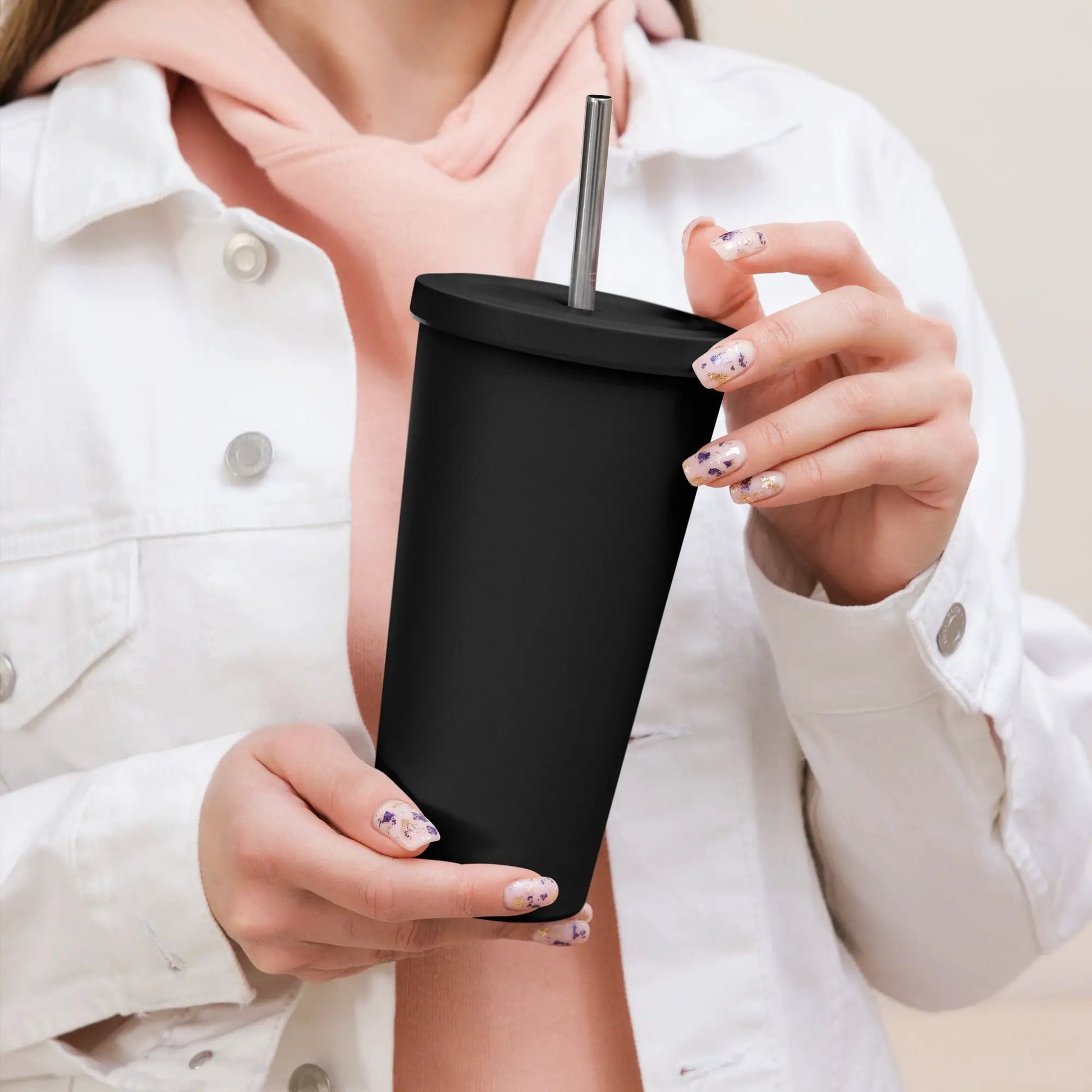 Insulated black tumbler with a metal straw, held by a person wearing a white jacket over a pink top.