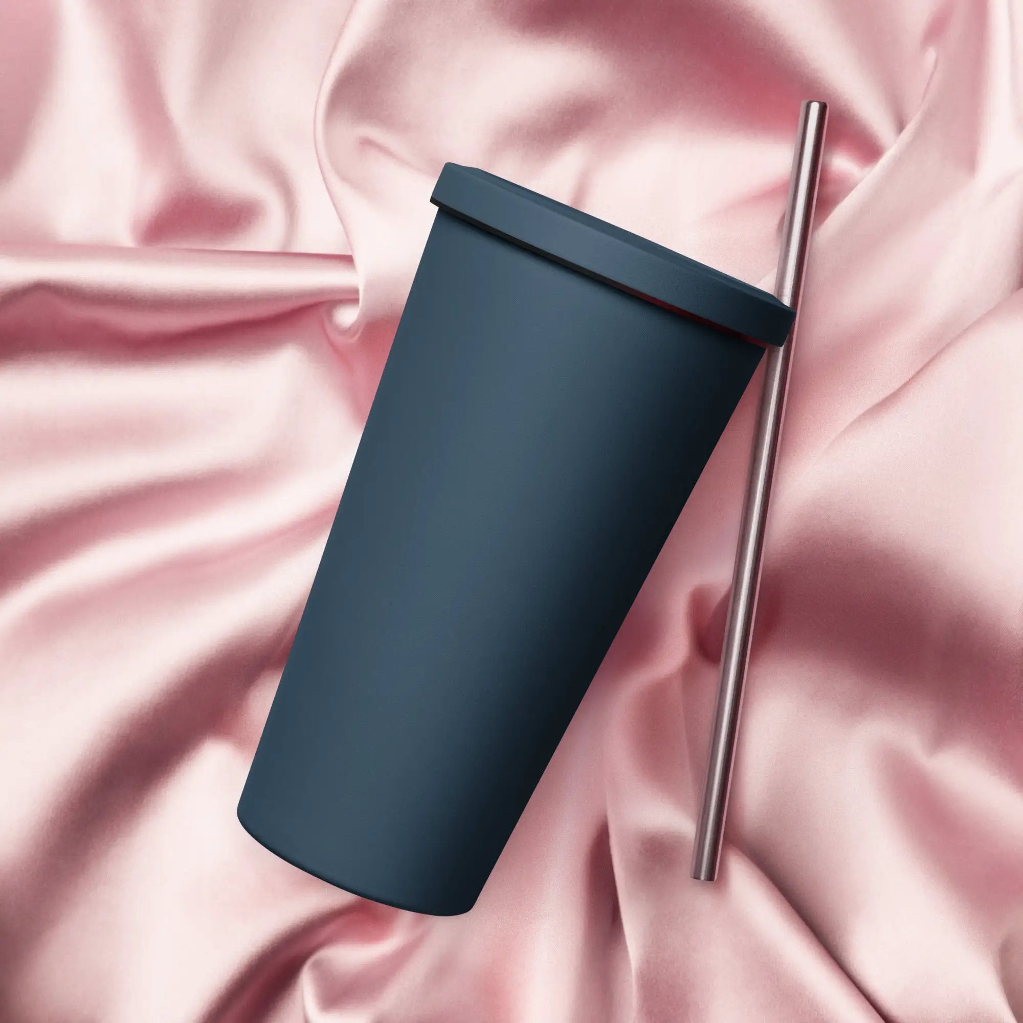 Dark blue insulated tumbler with a silver straw on pink satin background