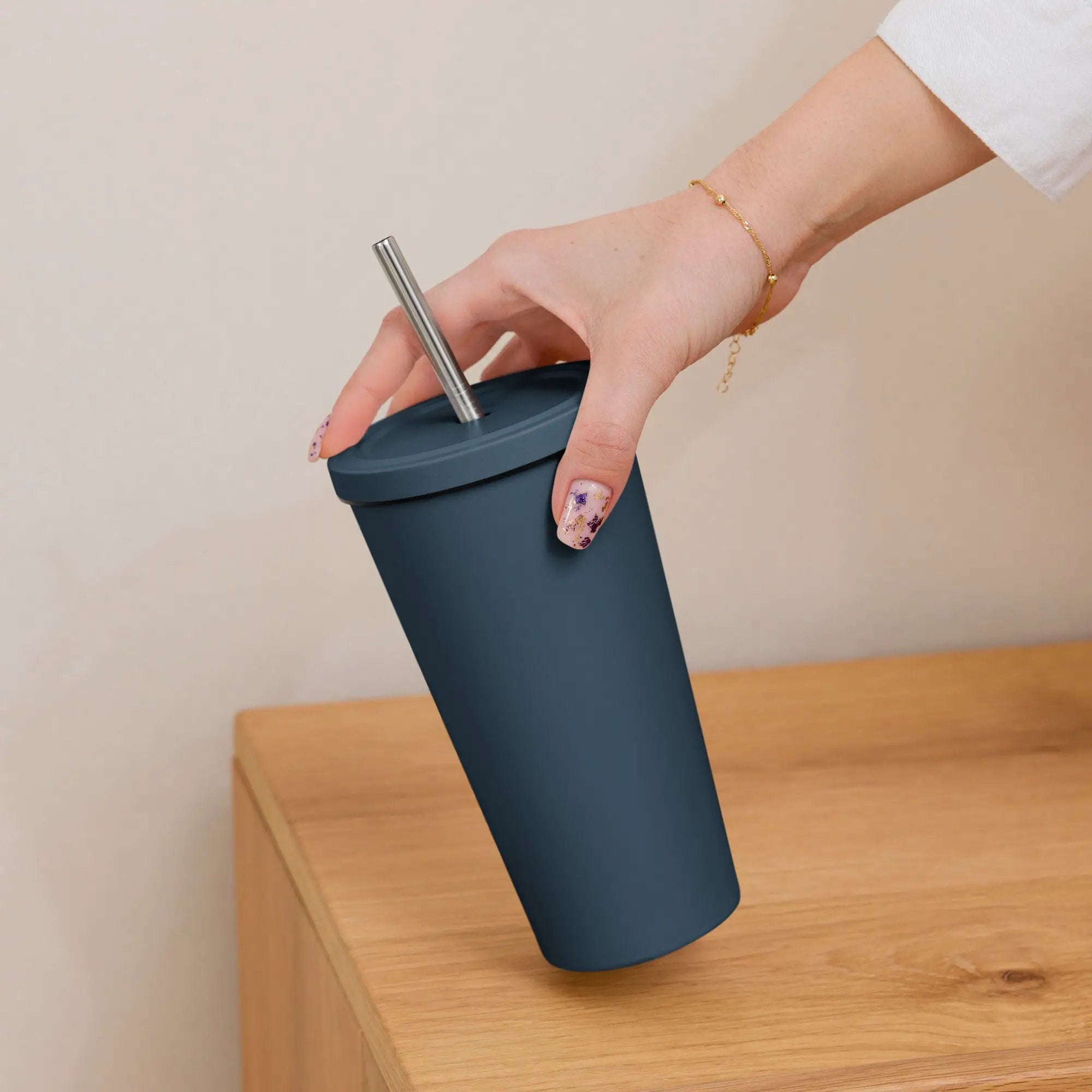 Insulated tumbler with stainless steel straw in navy blue, held by a hand with a gold bracelet