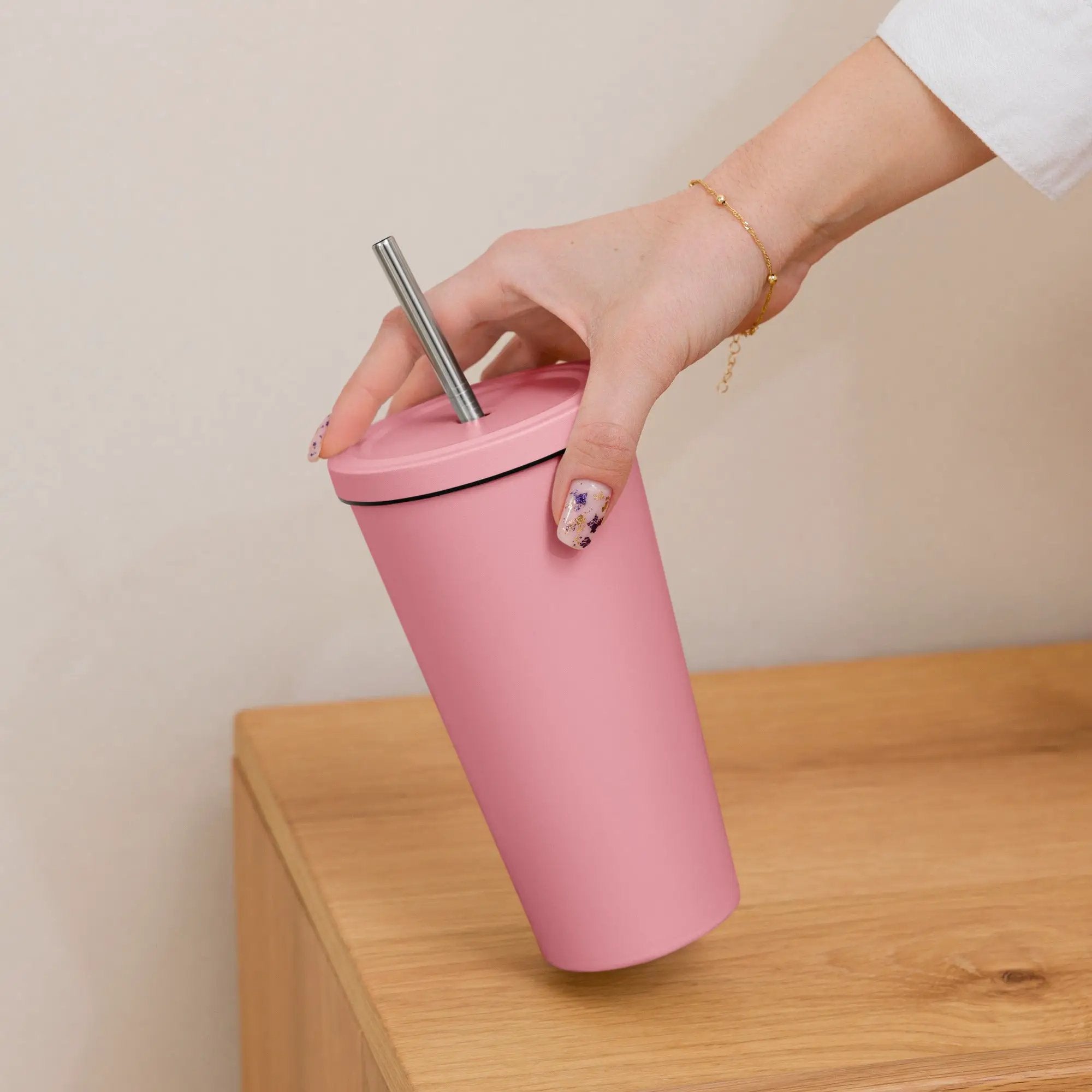 Pink insulated tumbler with straw, held by a hand wearing a gold bracelet.
