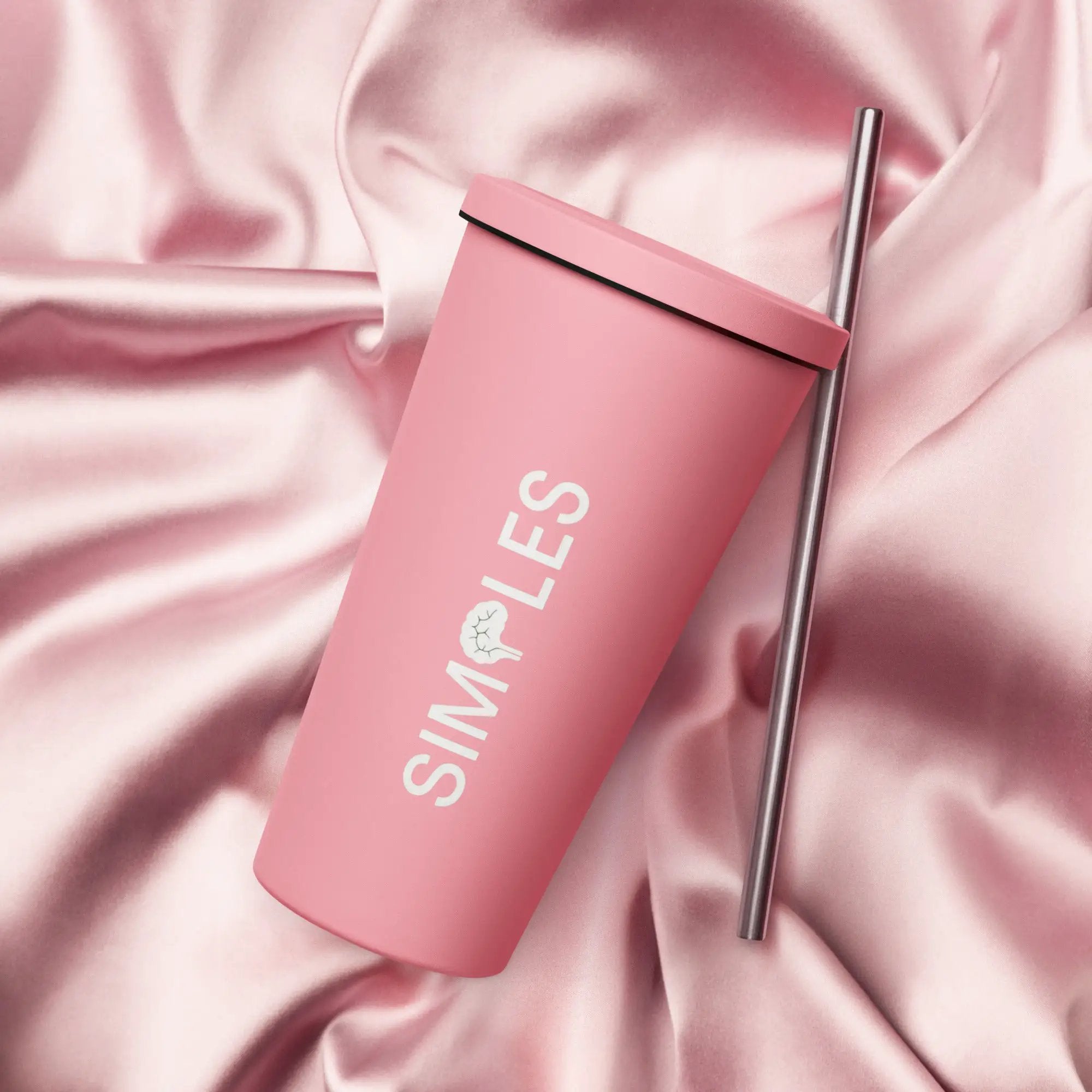 Insulated pink tumbler with a straw on pink satin background.