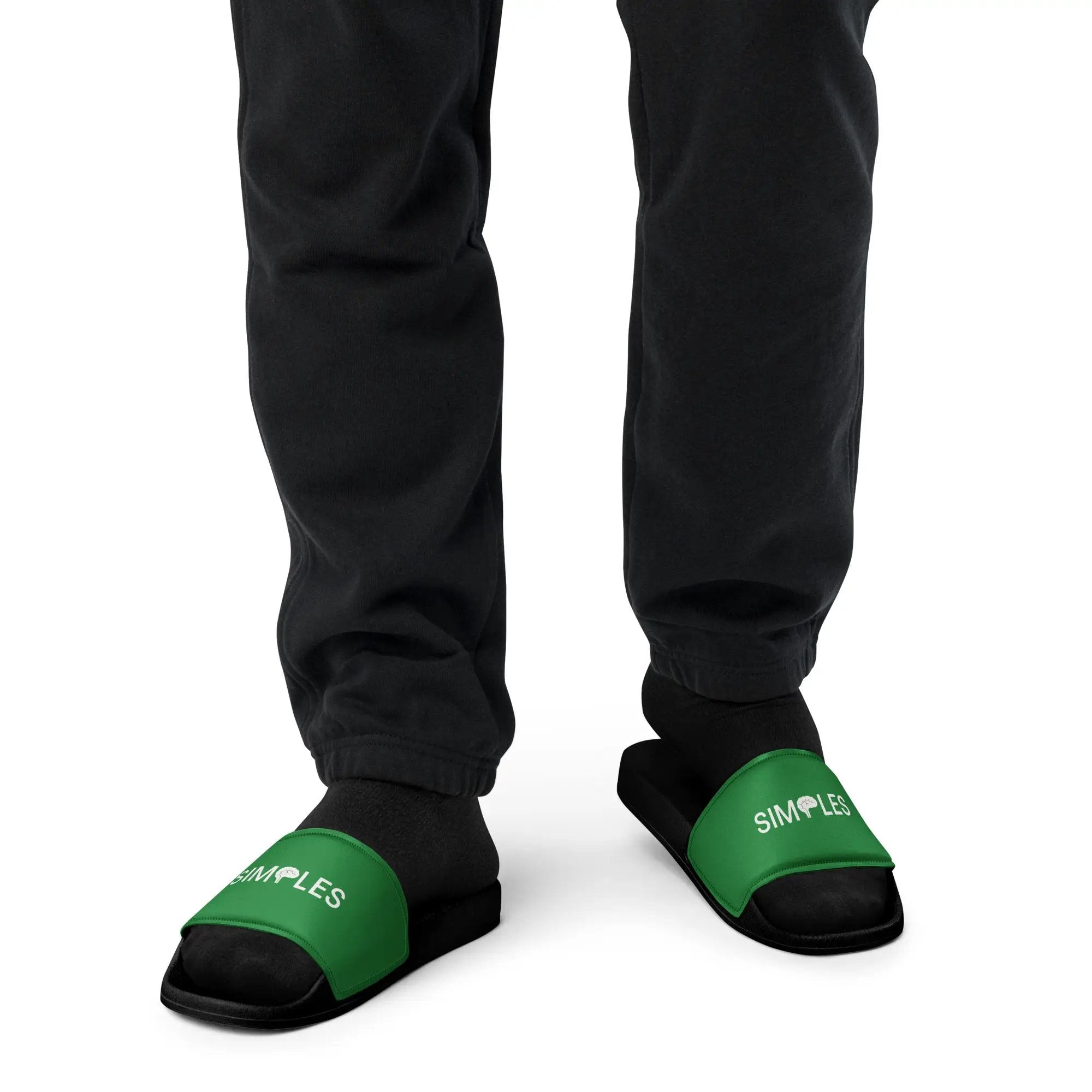 Men's slides by Simples Market, green straps with white logo, shown as a pair on black pants
