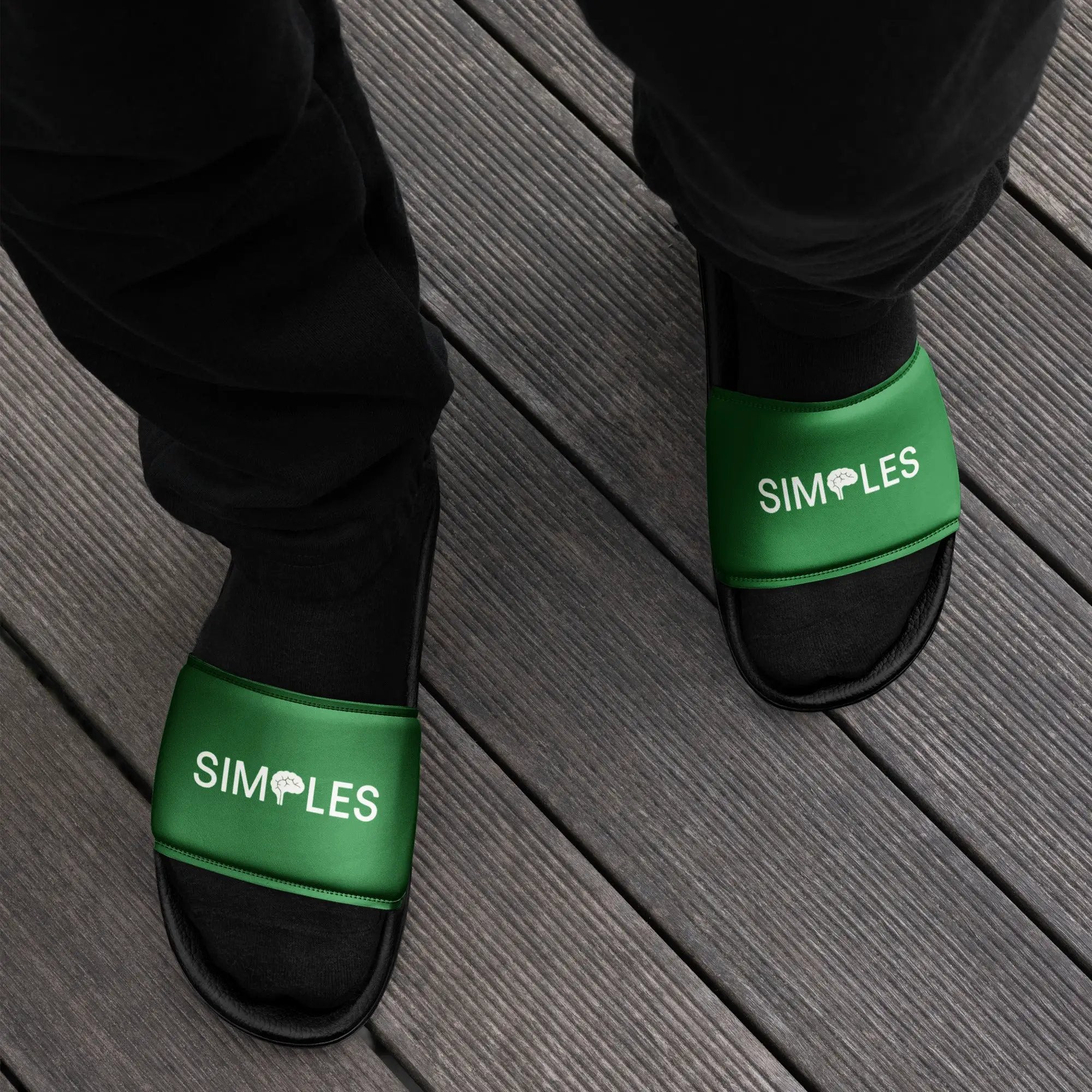 Men’s slides by Simples Market, 2 green-strapped black slides on a wooden deck
