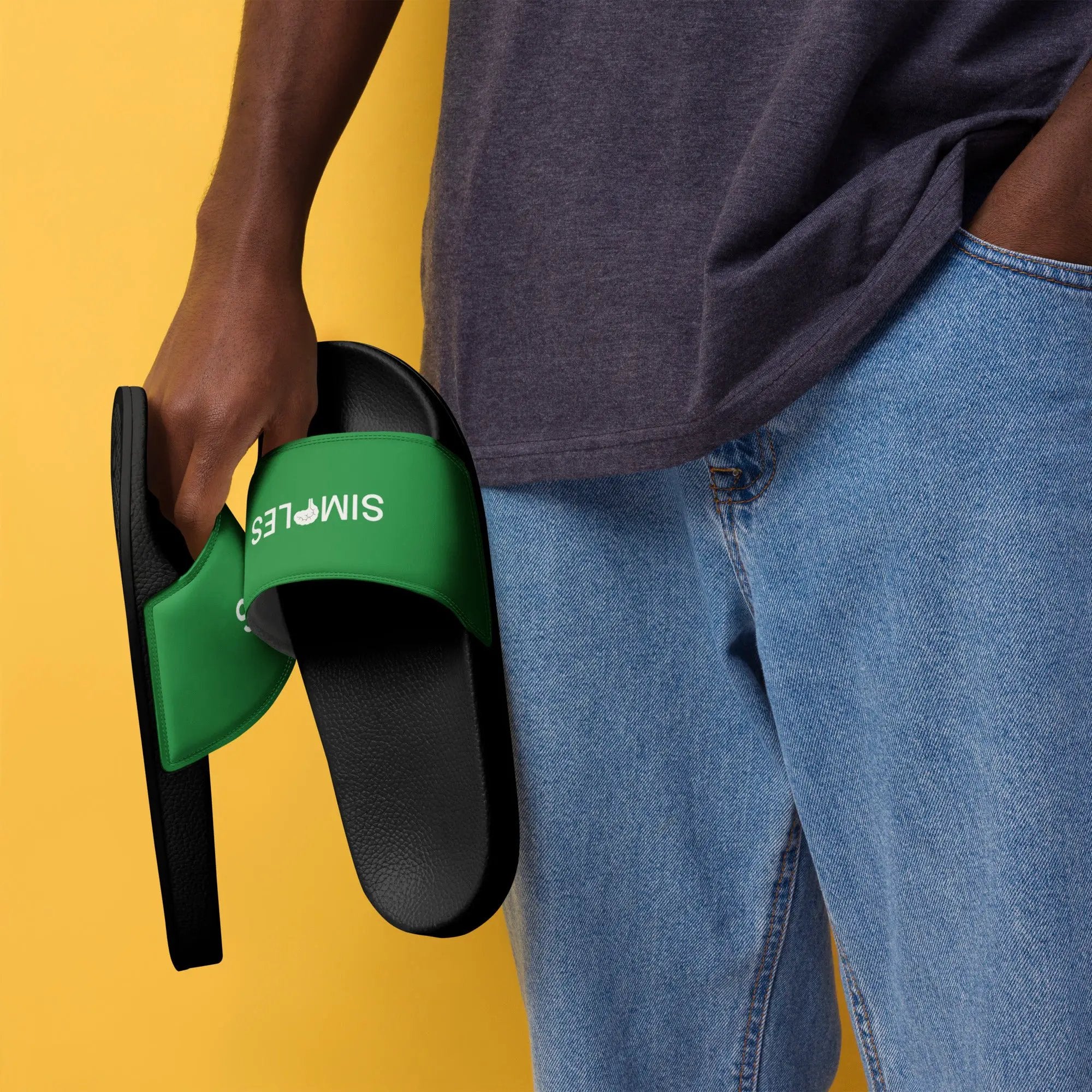 Men’s Slides by Simples Market; green strap over black sole, held by a person in denim jeans.
